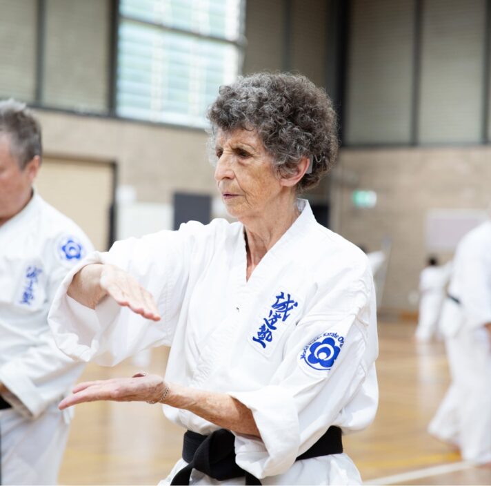 Two people at an indoor karate class. Both are in a karate uniform and are holding their hands in a karate pose.