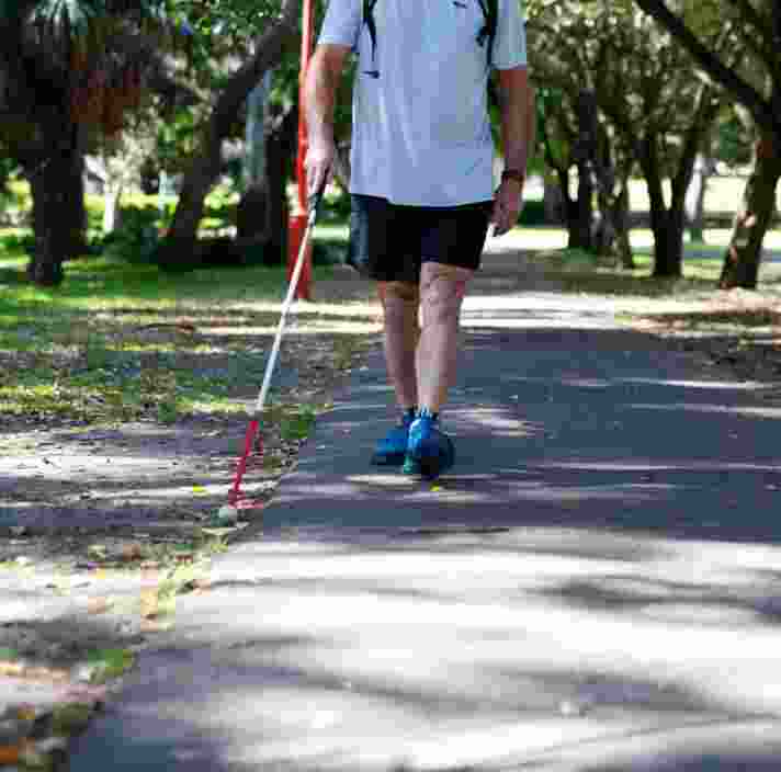 A person using their white cane while walking down a path in a park.