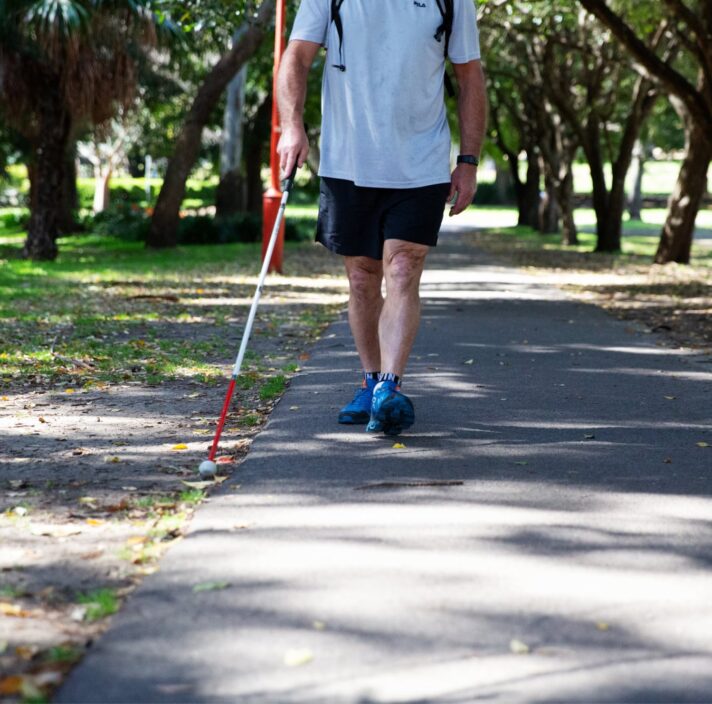 A person using their white cane while walking down a path in a park.