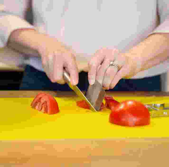 Person's hands chopping some tomatoes on a yellow chopping board.