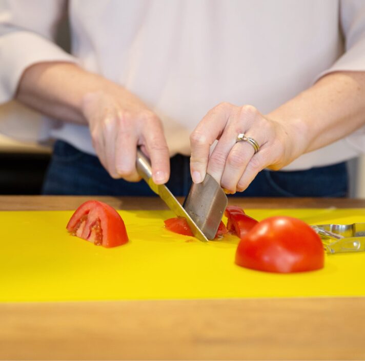 Person's hands chopping some tomatoes on a yellow chopping board.