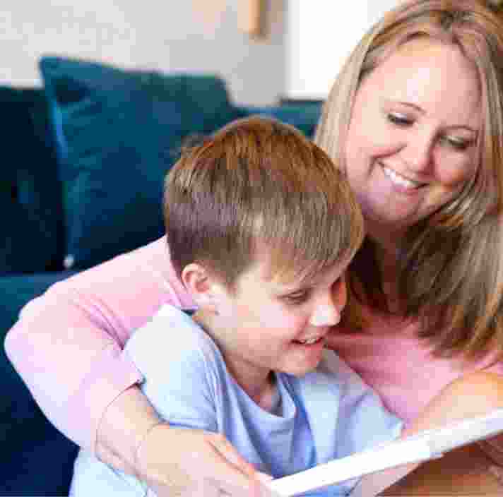 A woman wraps her arms around a young boy as they read a book together