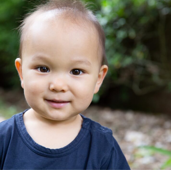 A young baby looking at the camera with a small smile on their face.