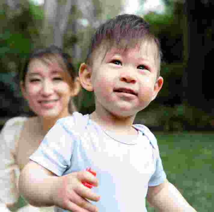 A young child playing outside with the mother watching in the background.
