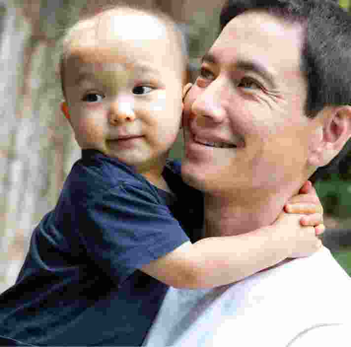 A father holding his toddler. The father has a smile on his face