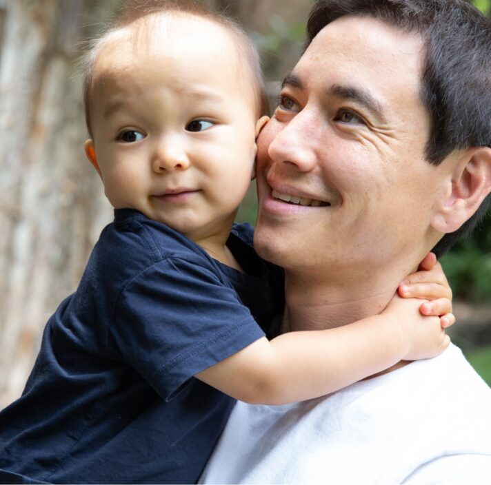 A father holding his toddler. The father has a smile on his face