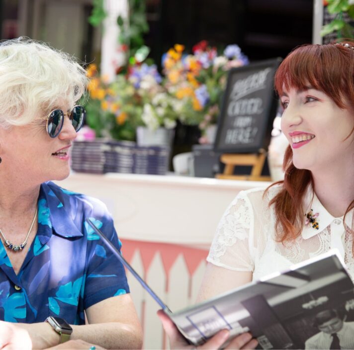 Two people sitting at a cafe looking at each other. They are both smiling and one is holding a menu.