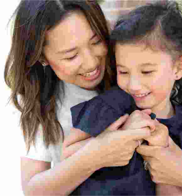 A mother and young child embrace. The mother is cuddling her child from behind.