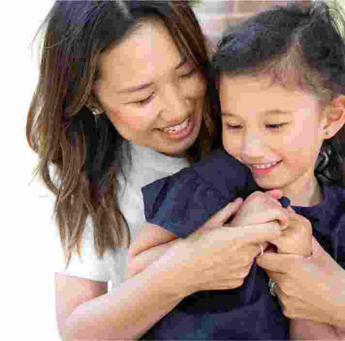 A mother and young child embrace. The mother is cuddling her child from behind.