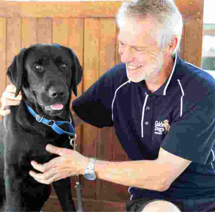A man smiles at a black Labrador