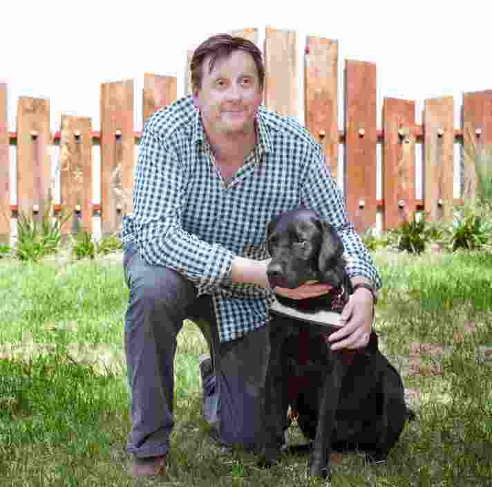 A person kneeling down outside next to a black labrador Guide Dog in harness.