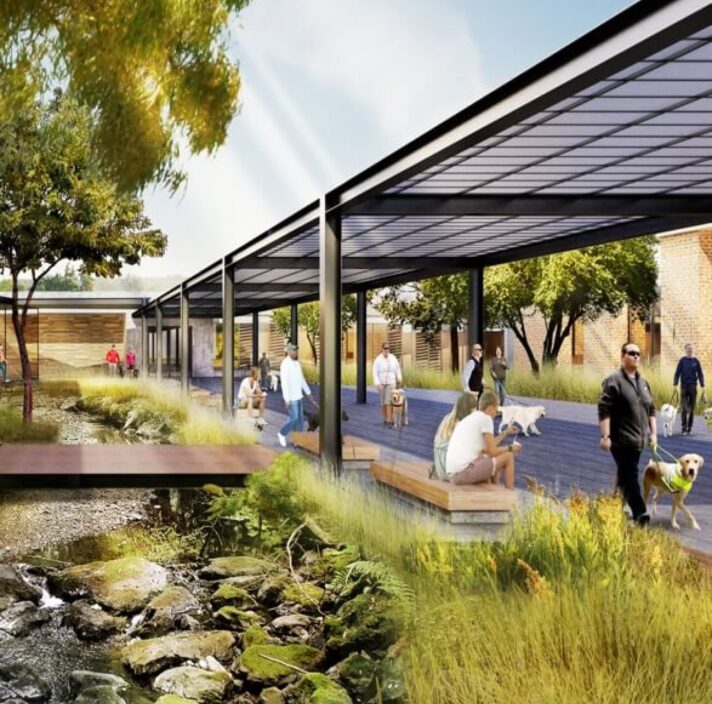 A render of a building with an outside footpath that is covered, next to a small stream with pebbles in it. Across the stream is a wooden bridge.
