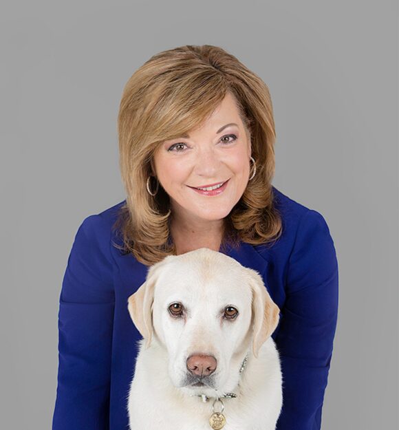 Guide Dogs Victoria Chief Executive Officer, Karen Hayes with a yellow labrador dog. Karen is behind the dog and both are looking at the camera.