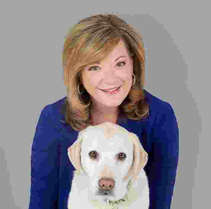 Guide Dogs Victoria Chief Executive Officer, Karen Hayes with a yellow labrador dog. Karen is behind the dog and both are looking at the camera.
