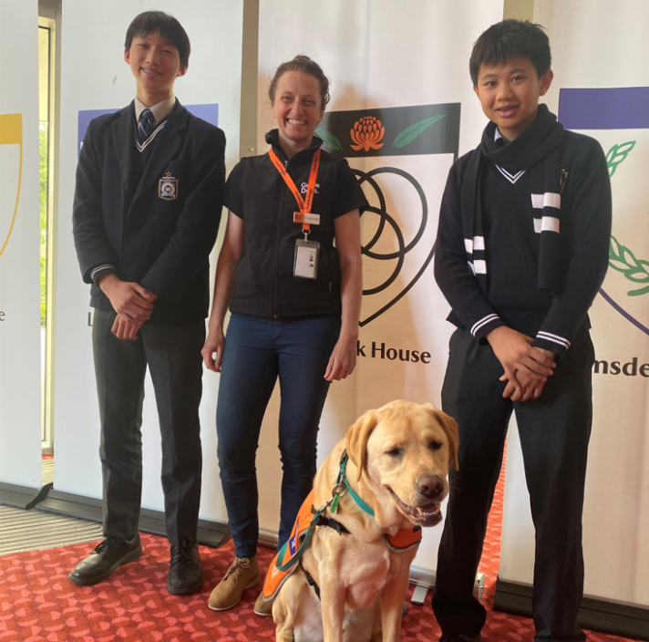 Two students stand next to a Guide Dogs staff member and Ambassador Dog Rafa