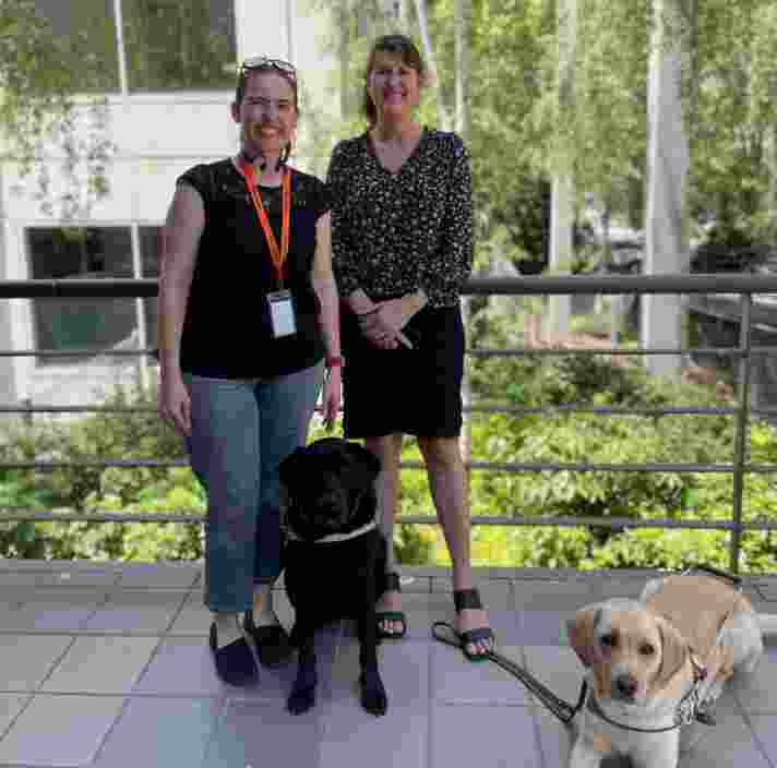 Erin and Melaine standing on a balcony with their Guide Dogs in front of them