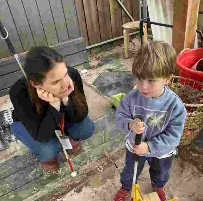 Guide Dogs staff member, Erin, kneeling down with her head in her hands, listening intently as Louie talks to her about his white cane, Sneezy.