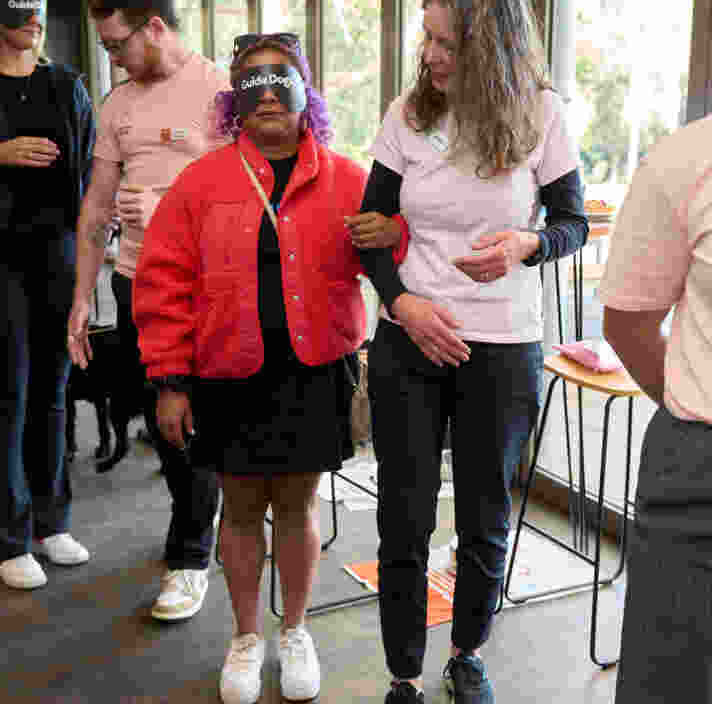A guest wearing a red coat is being guided by an event volunteer to experience how to walk after completely losing vision.